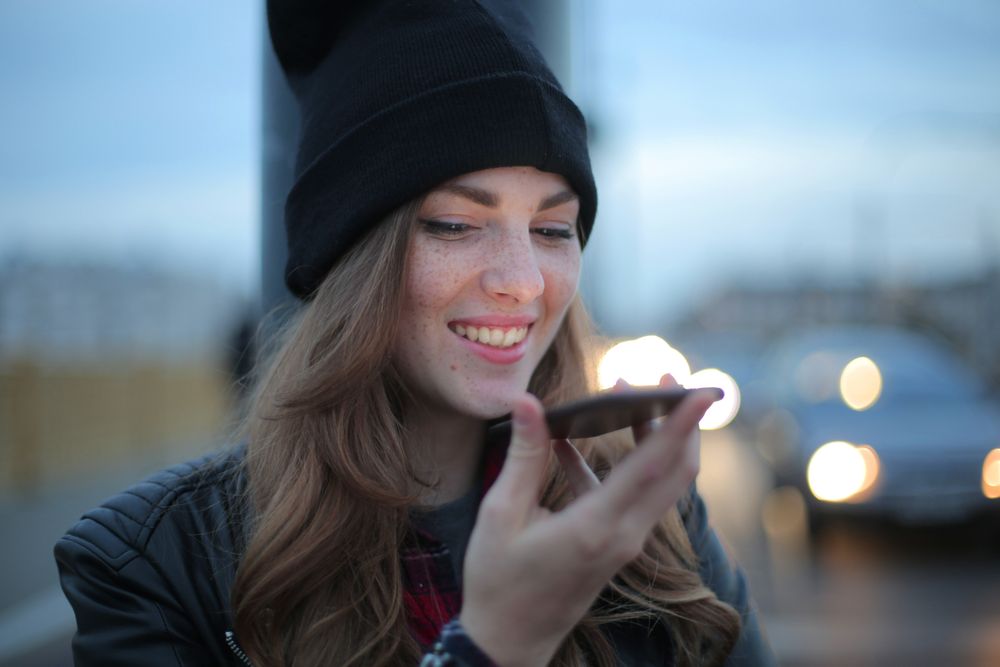 Jeune femme souriante enregistrant un message vocal sur son smartphone, comme les nouveaux commentaires vocaux de TikTok