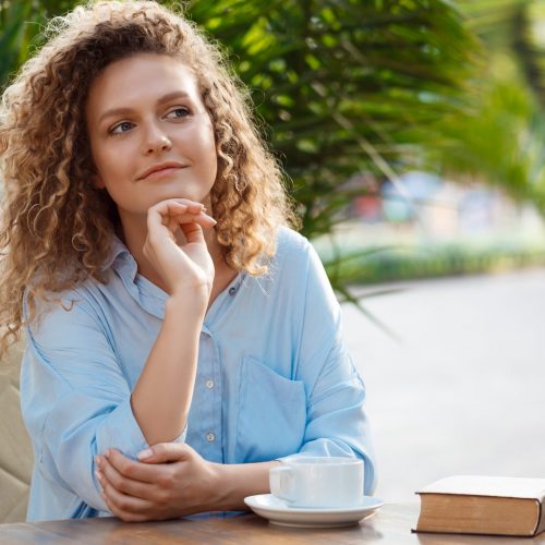 Young beautiful girl sitting in cafe. Young beautiful girl smiling, holding cup of coffee, sitting in cafe.